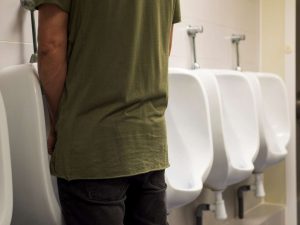 גבר עומד מול משתנה בשירותים ציבוריים, להמחשת תסמיני ערמונית או בעיות במתן שתן